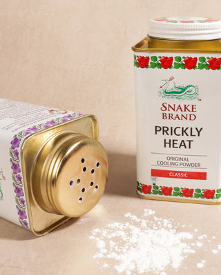 Photo shows two cans of Snake Brand powder, to the left there is an lavender tin and to the right is the classic tin. There is some powder below.