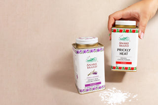 Photo shows two cans of Snake Brand powder, to the left there is an lavender tin and to the right is the classic tin. There is some powder below.